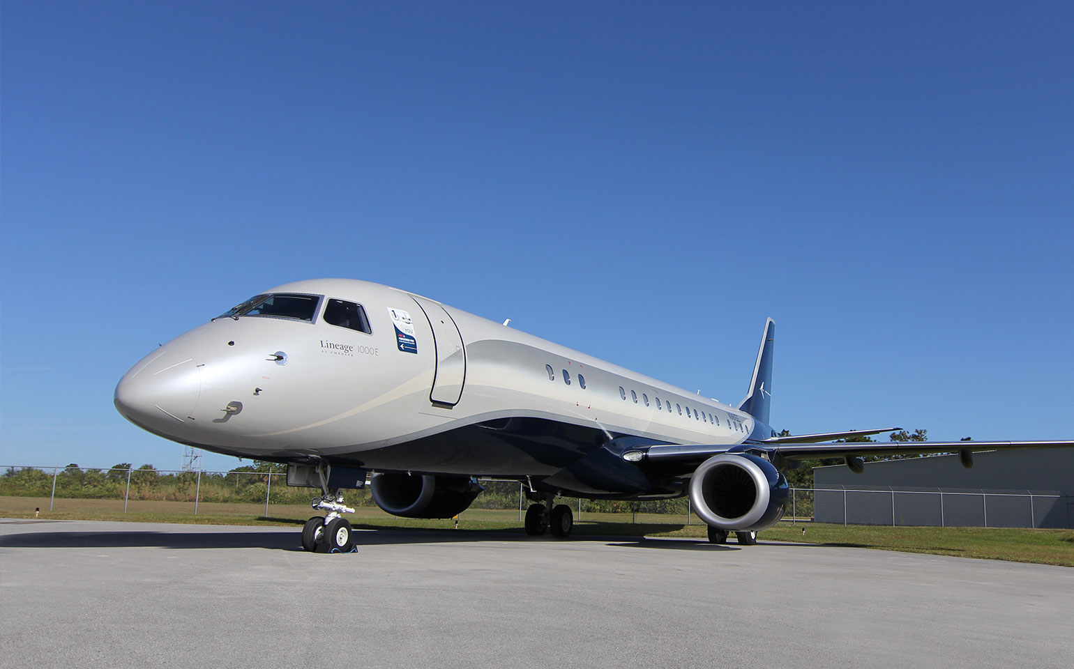 Embraer Lineage 1000 private jet charter parked by airport and grass